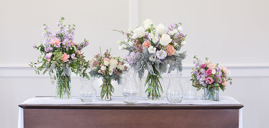 A table with several different vases and pastel colored floral arrangements.