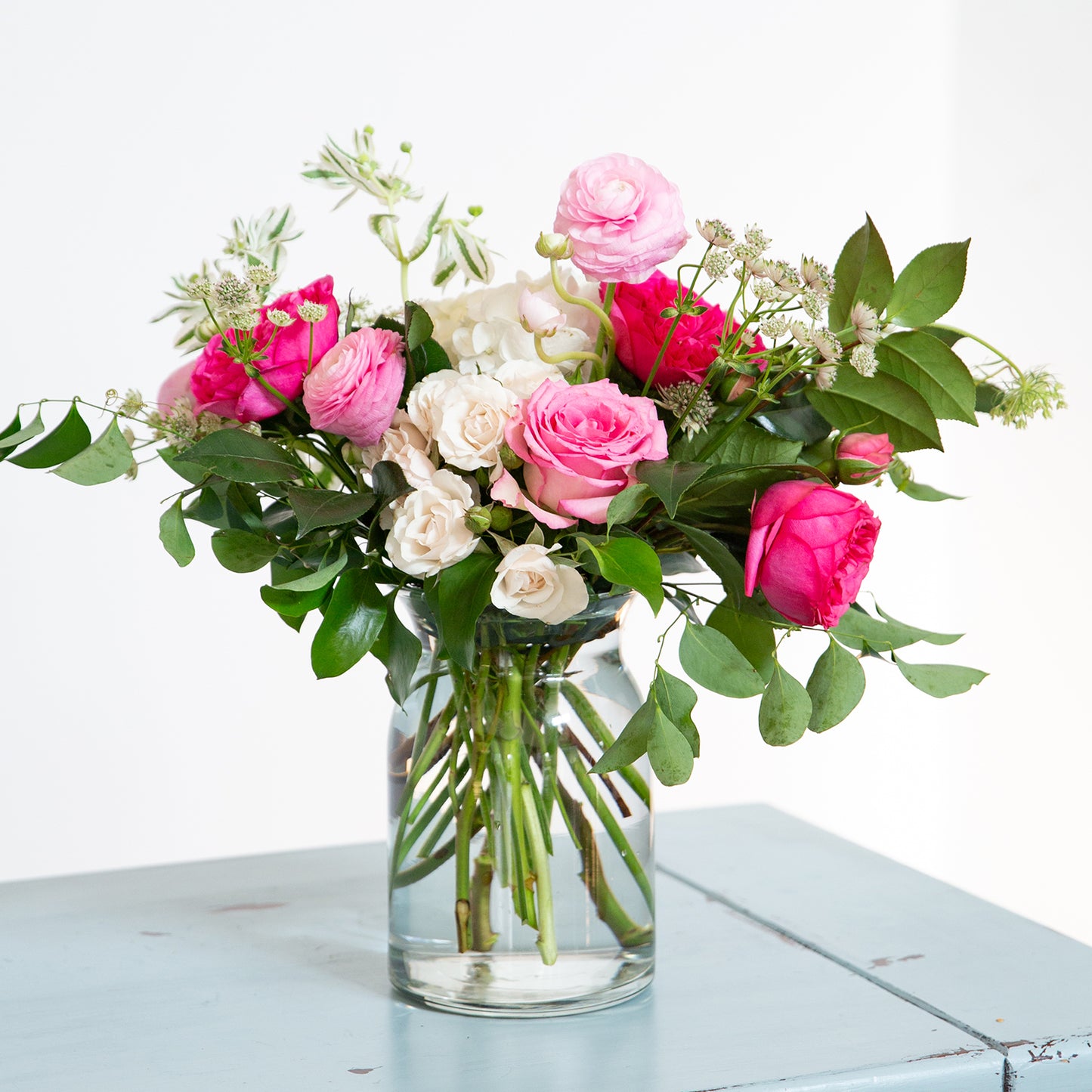 Pink, red, and white roses arranged beautifully in a milk jug vase.