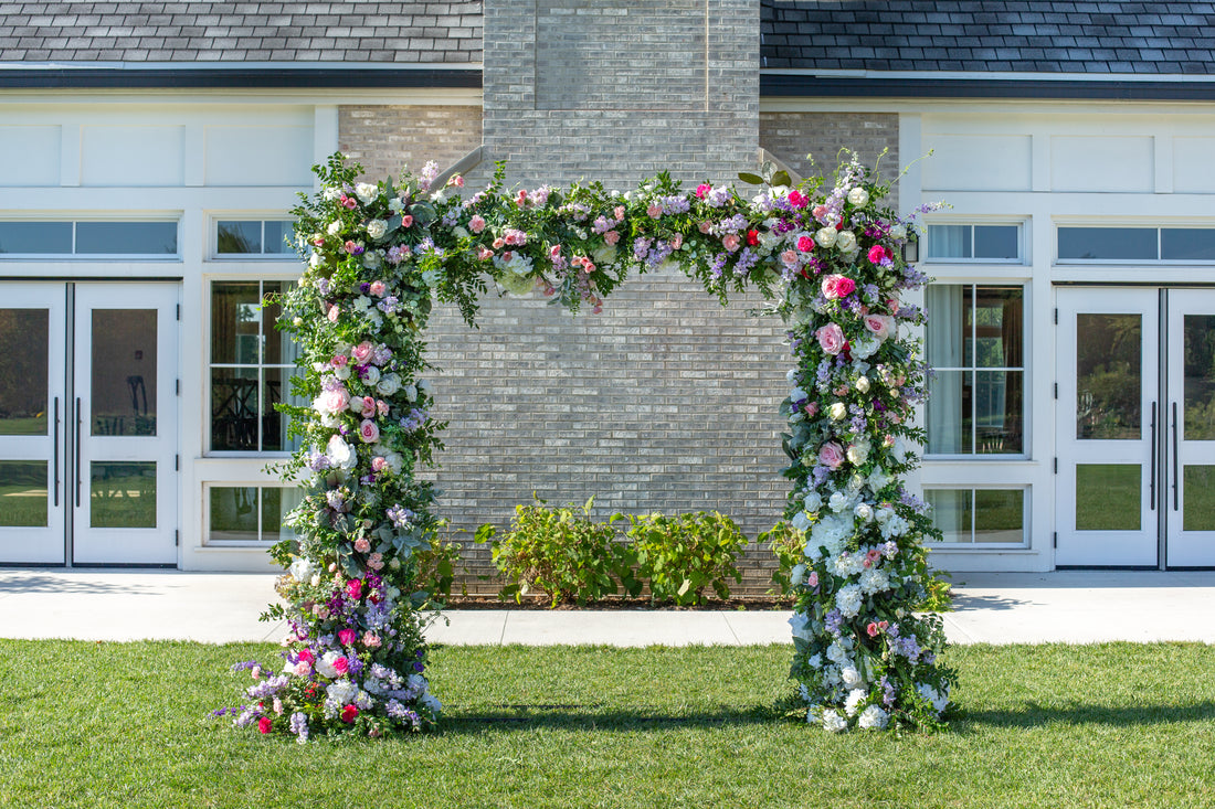 A square wedding arch covered in flowers and greenery outside a building