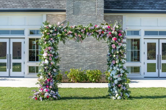 A square wedding arch covered in flowers and greenery outside a building