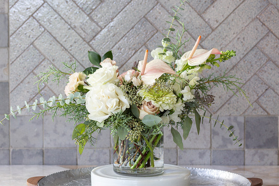 A clear vase with green and peach flowers arranged in it 