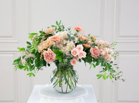 A bouquet of peach-colored flowers in a large clear glass vase