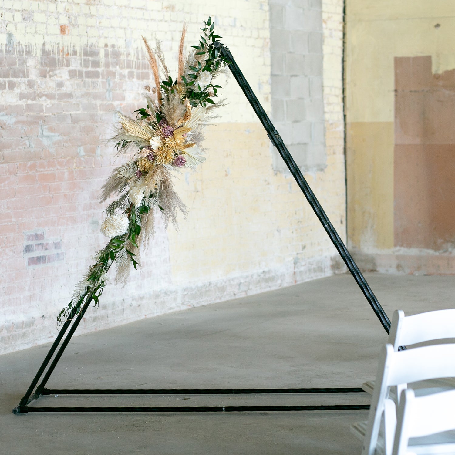 Elegant wedding arch in a triangle shape with hanging greenery. - 46 & Spruce