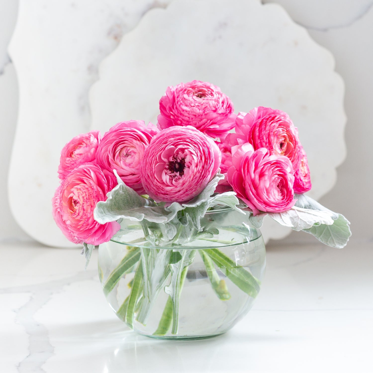 Vibrant pink ranunculus flowers in a recycled glass bubble ball vase on marble surface