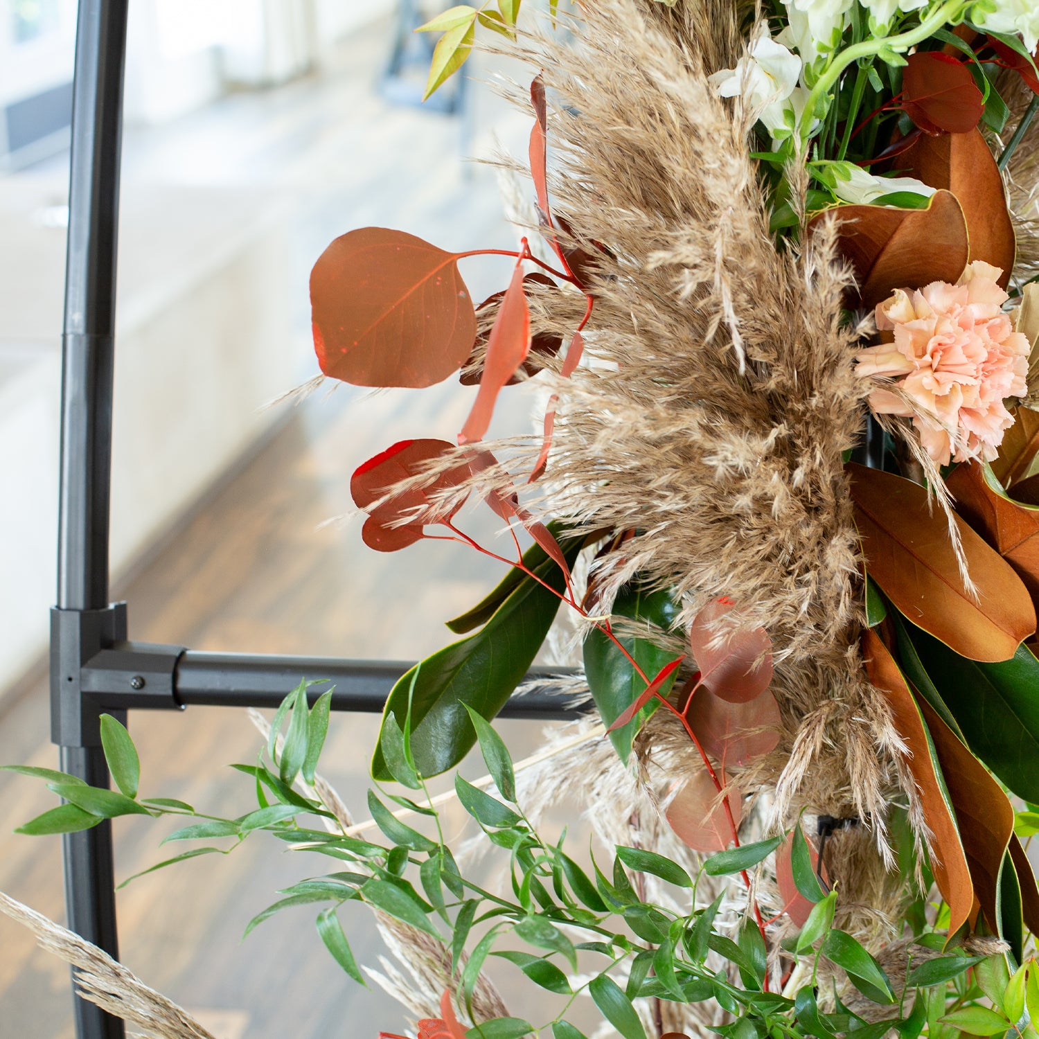 46 & Spruce round arch close-up: detail of pampas grass, eucalyptus leaves, and peach-colored flowers. Elegant texture and natural tones for a sophisticated look.
