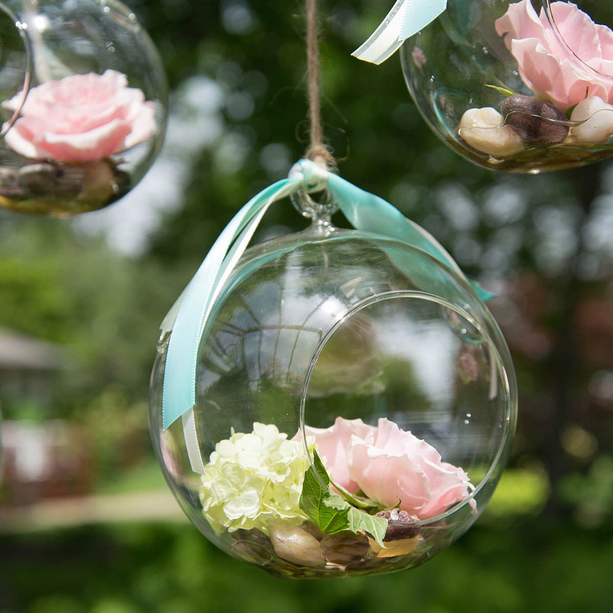 medium round hanging terrarium filled with flowers and stones hanging outside